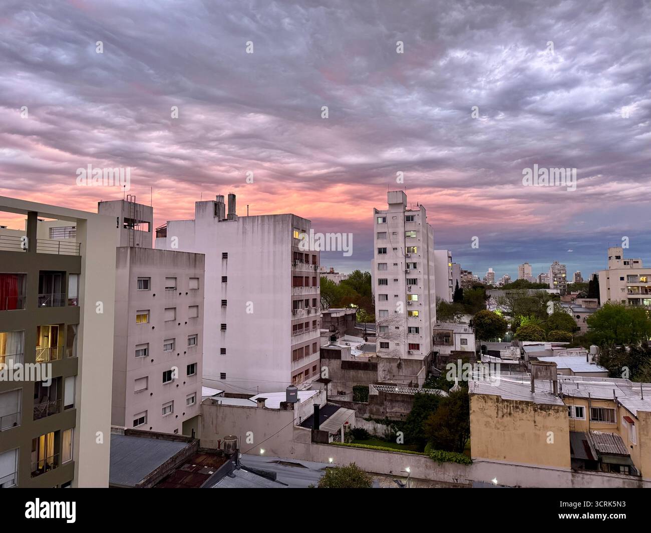 Un paysage urbain avec des immeubles d'appartements de hauteur moyenne et des maisons entourées d'arbres sous un ciel nuageux spectaculaire et coloré au coucher du soleil. - Image de stock capturée avec un smartphone