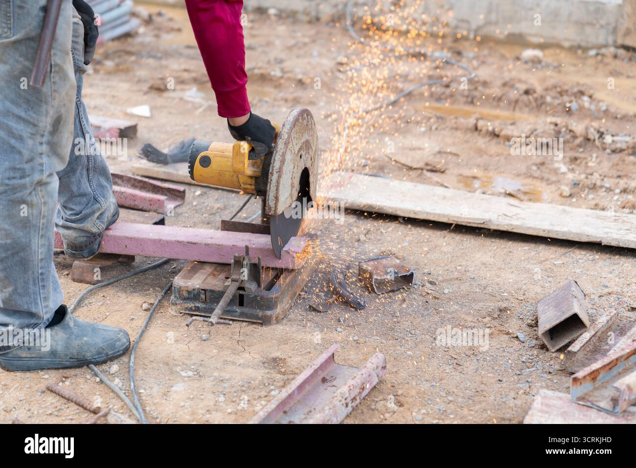 Gros plan d'un ouvrier de la construction utilisant une scie à tronçonner portative sur un chantier extérieur. La puissante lame abrasive coupe à travers un I-b en acier Banque D'Images
