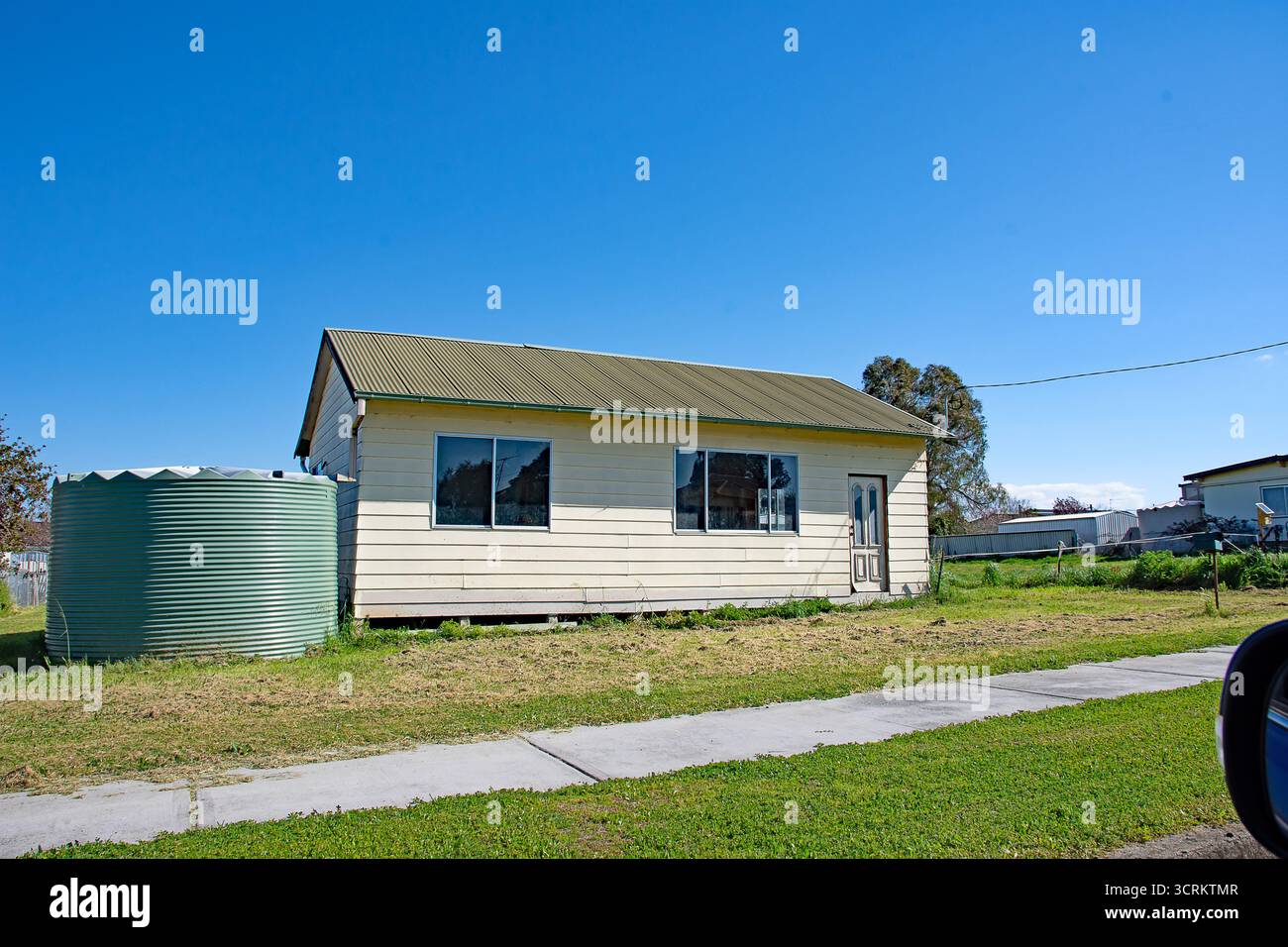 Une maison simple en plâtre avec toit à pignon en fer ondulé et grand réservoir d'eau de pluie dans la campagne de Nouvelle-Galles du Sud en Australie. Banque D'Images