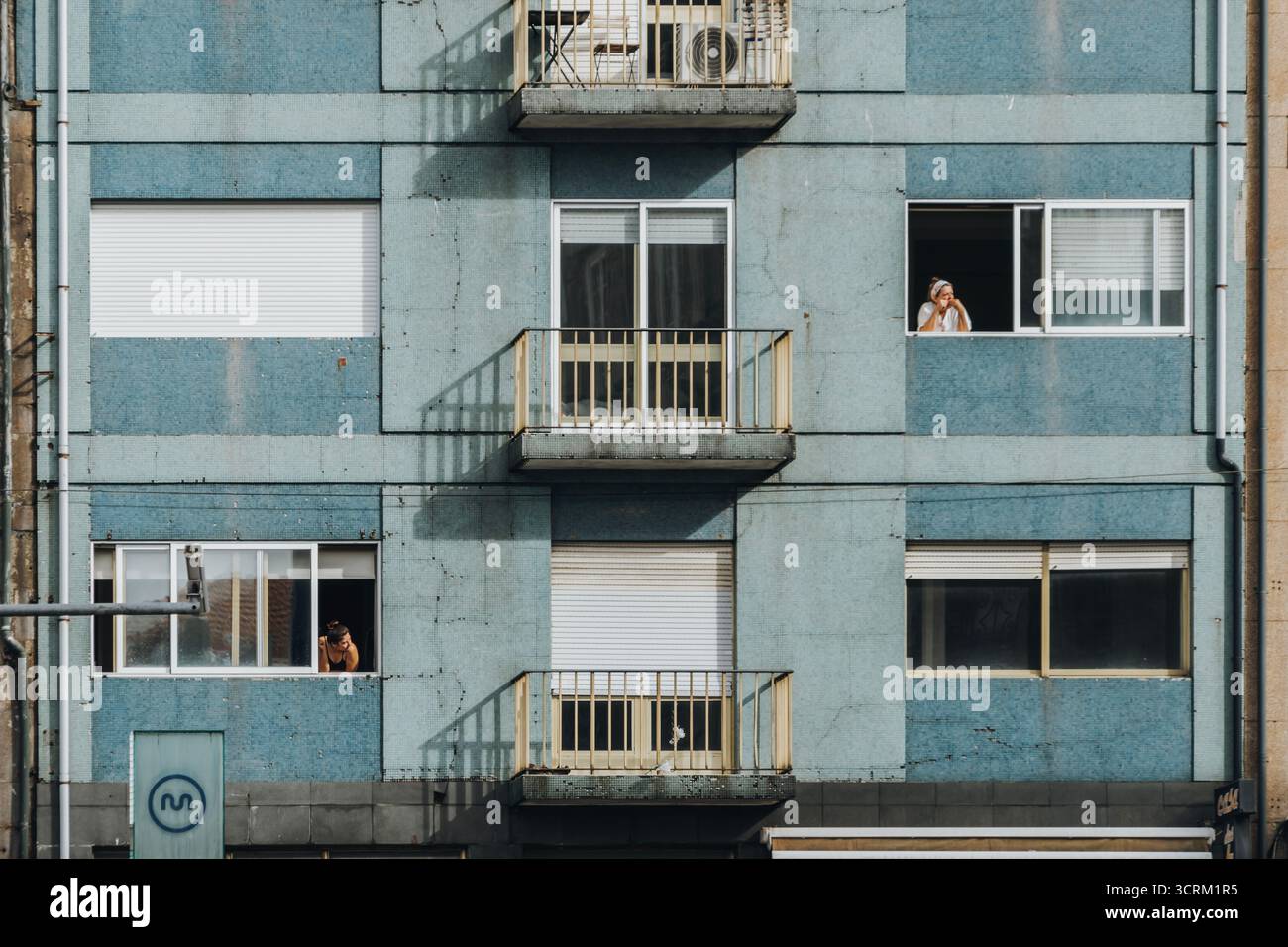 Vue rapprochée d'une façade de bâtiment résidentiel moderne peinte en bleu avec des balcons jaunes, où deux femmes regardent par les fenêtres dans une ville Banque D'Images