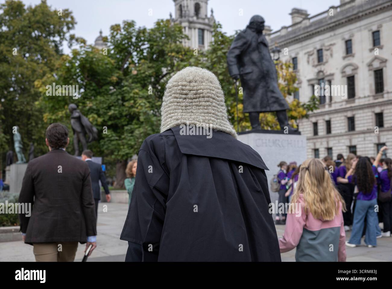 Un avocat vêtu d'une tenue de cour traditionnelle marche vers la statue de Winston Churchill située sur Parliament Square, au centre de Londres Banque D'Images