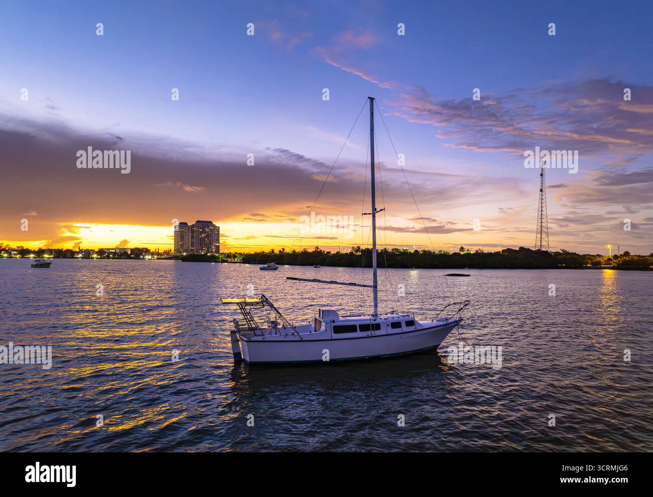 Vue aérienne d'un voilier solitaire flottant sur Biscayne Bay alors que le soleil couchant peint le ciel dans des teintes flamboyantes derrière les bâtiments, Miami, Floride, États-Unis. Banque D'Images