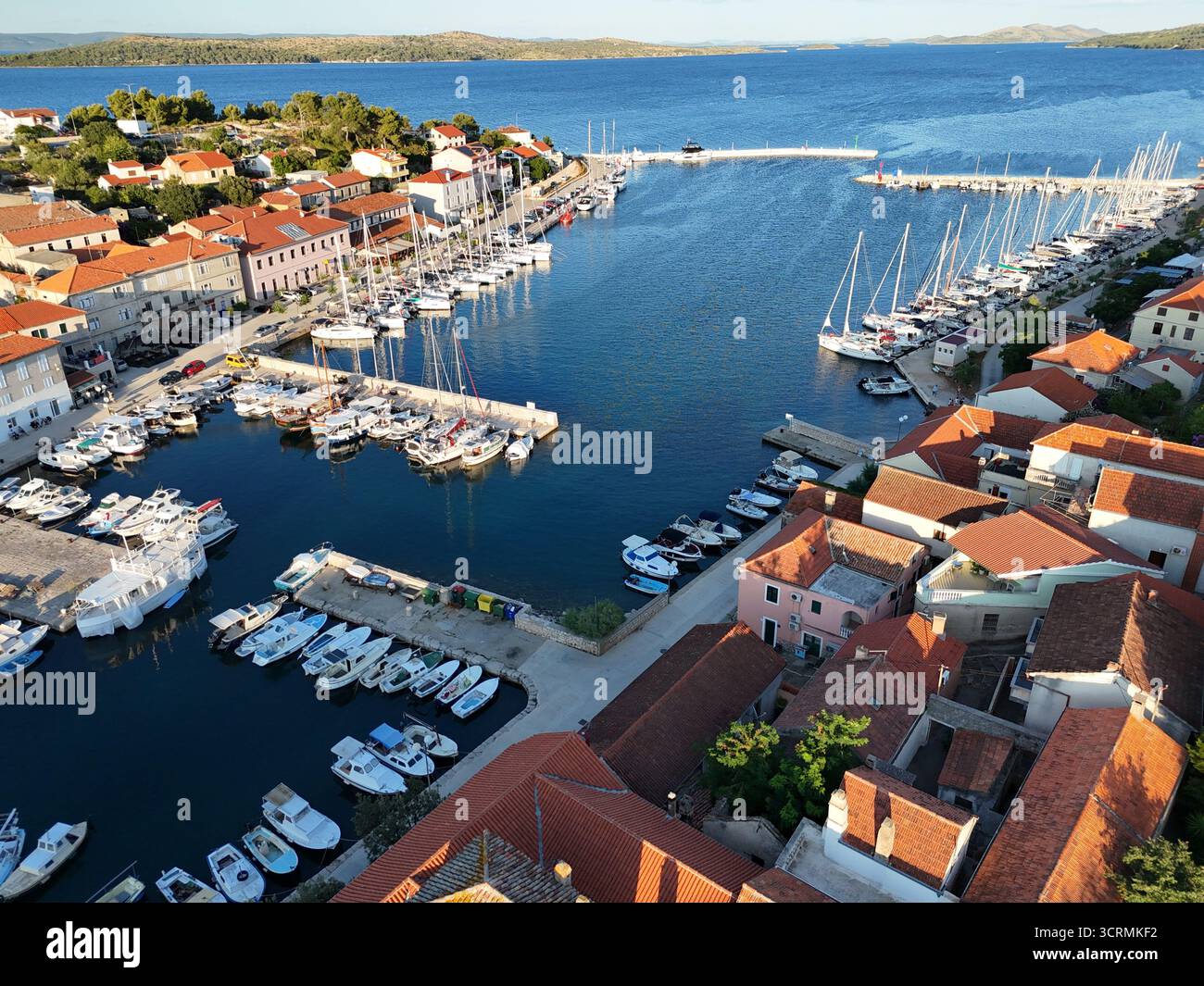 Vue aérienne des bateaux nichés dans un port serein, toits en terre cuite contrastant avec la mer bleu profond, créant une scène pittoresque, Dugi Otok, comté de Zadar, Croatie. Banque D'Images