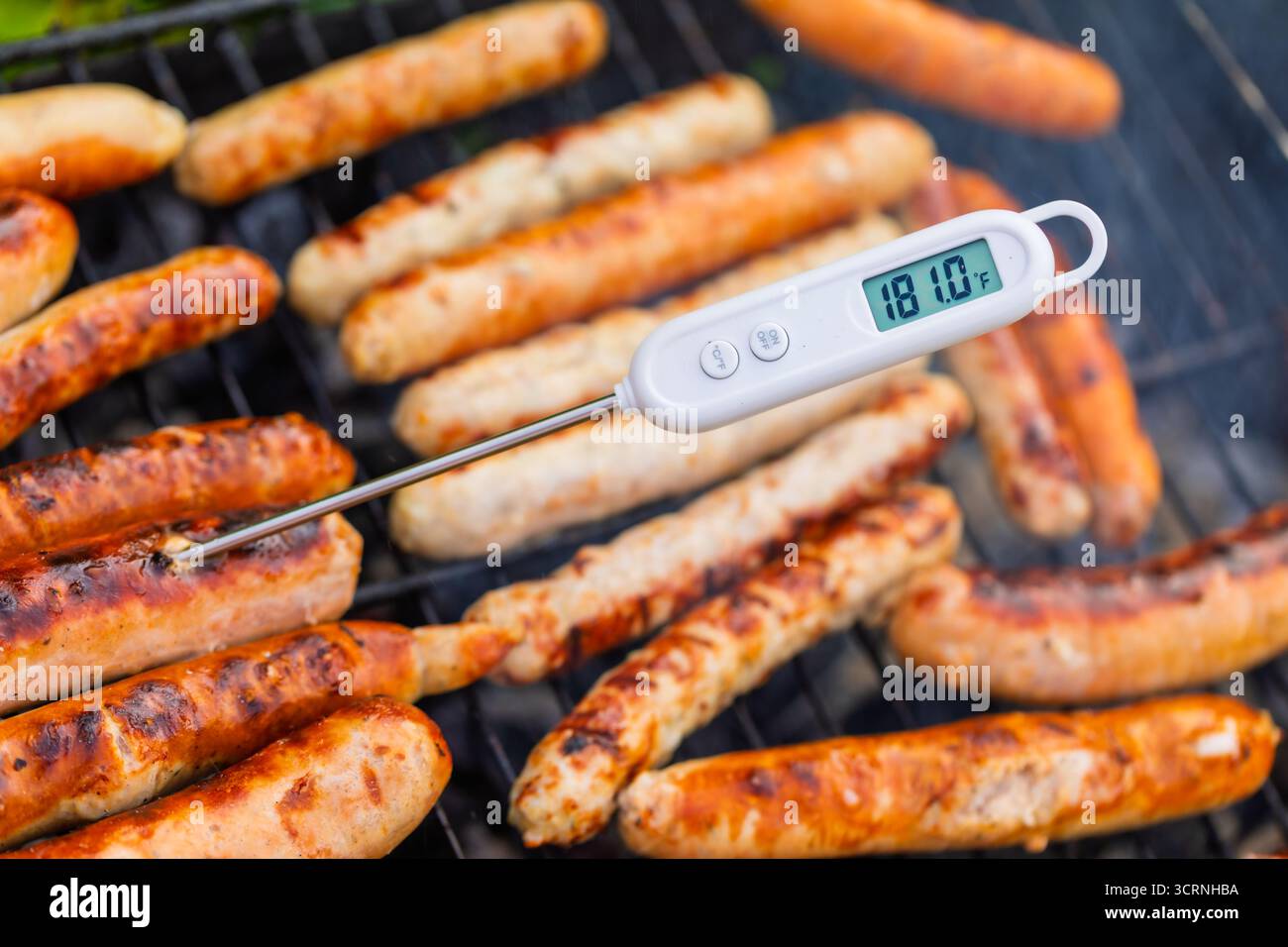 Gros plan de saucisses grillées sur un barbecue avec un thermomètre à viande numérique inséré, affichant 181F, une température indiquant une viande trop cuite au-delà Banque D'Images
