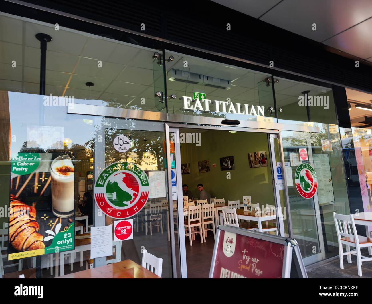 Manchester, Royaume-Uni - 25 septembre 2025 : vue sur la rue lumineuse d'un restaurant italien avec logo halal, façade en verre et salle à manger confortable. Banque D'Images