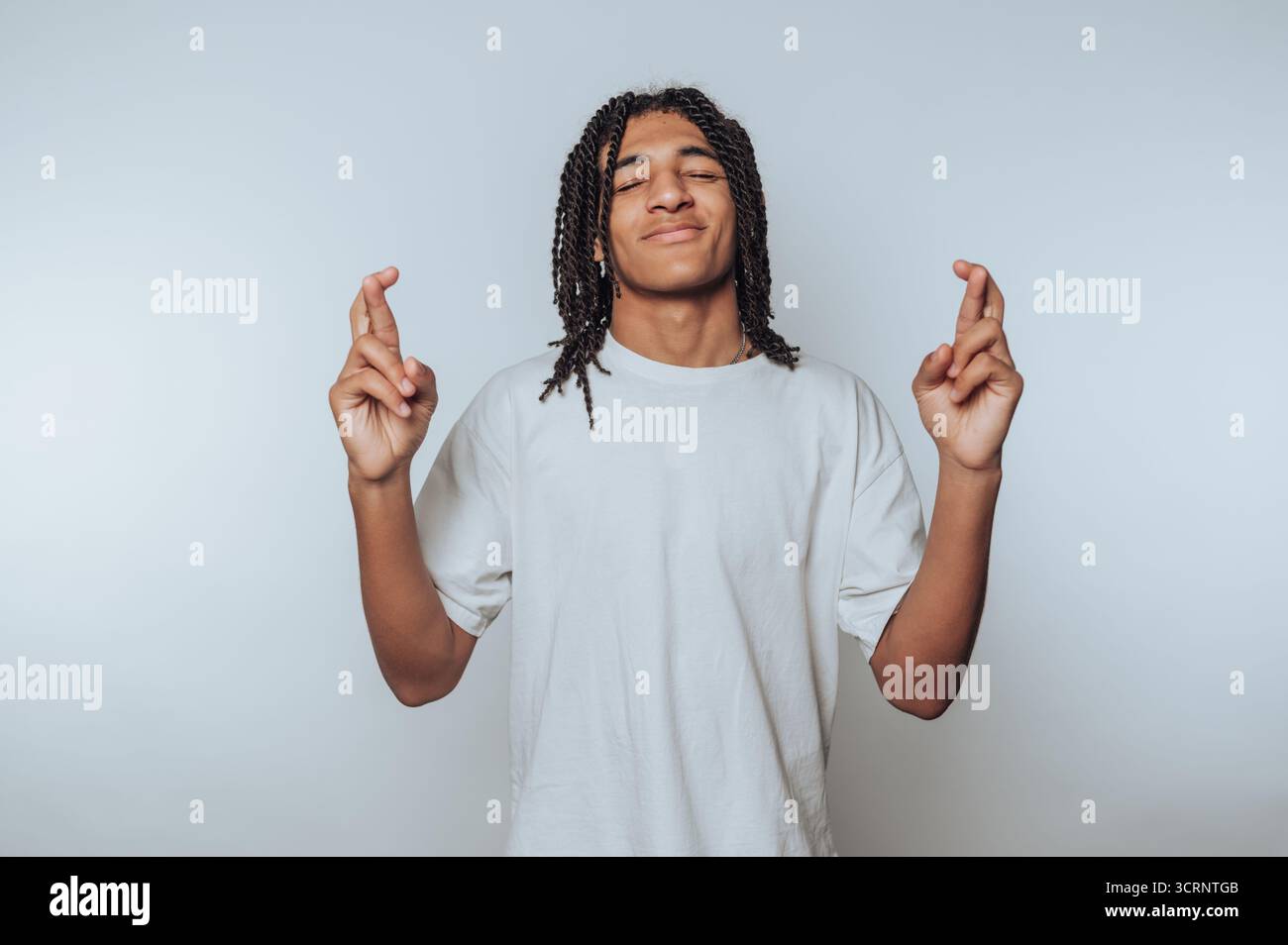 portrait du jeune homme sourit en croisant les doigts, symbolisant l'espoir et souhaitant bonne chance sur fond clair Banque D'Images
