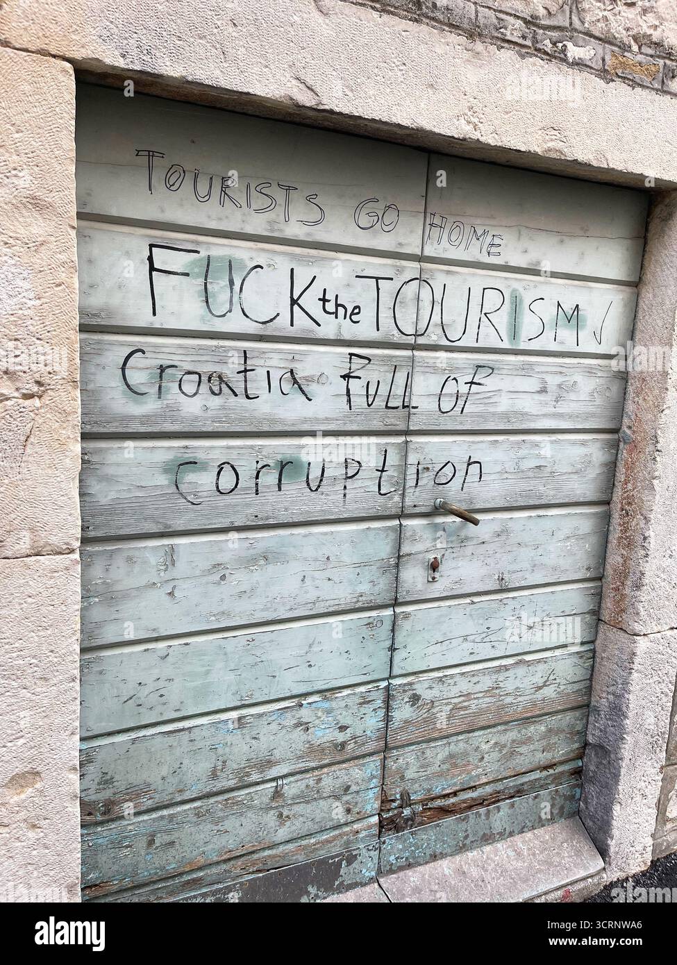 Graffiti sur une porte croate proteste contre le tourisme et la corruption, reflétant le mécontentement local et les tensions sociopolitiques dans l'espace urbain Banque D'Images