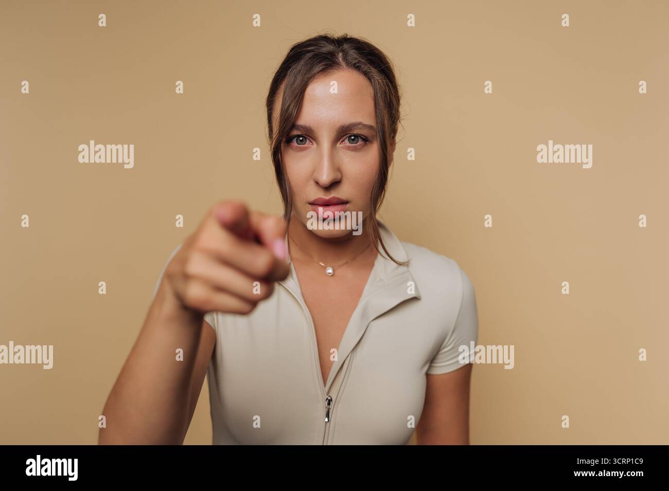 Une femme avec une expression sérieuse pointe directement vers le spectateur, montrant la confiance et l'affirmation de soi. L'arrière-plan neutre souligne son focuse Banque D'Images