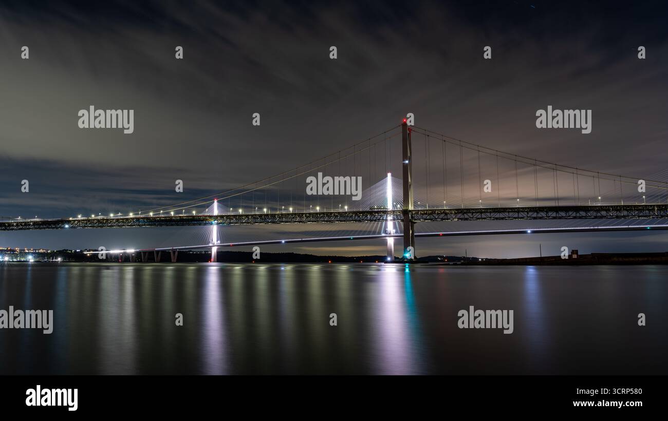 Queensferry Crossing, un pont à haubans moderne enjambant Firth of Forth, illuminé de nuit, reflétant ses lumières sur l'eau plate Banque D'Images