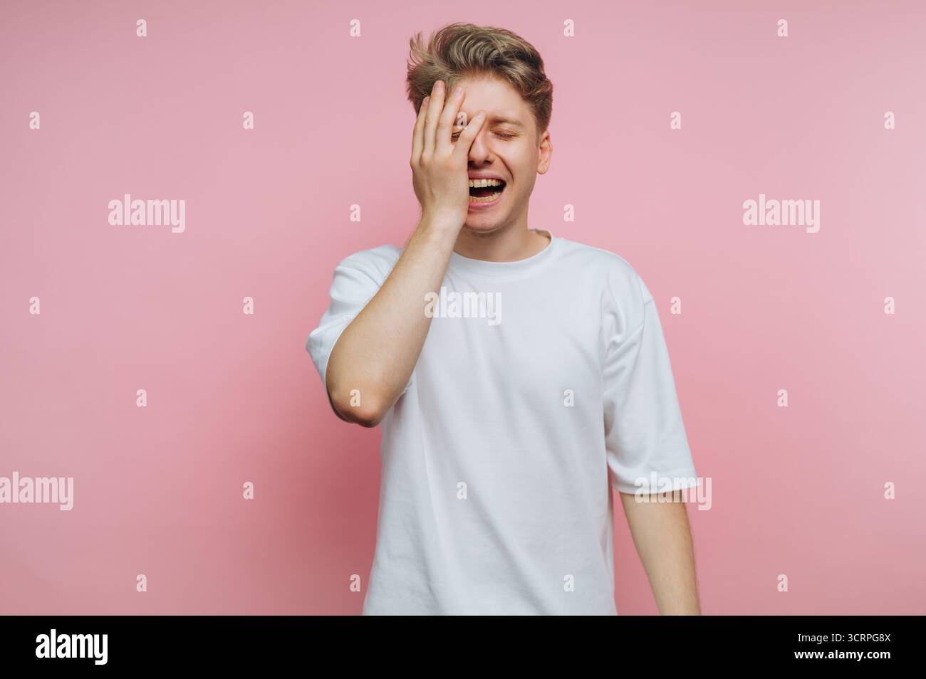 portrait d'un jeune homme en détresse cache son visage dans la frustration, dépeignant la profondeur de la déception et de la lutte émotionnelle sur fond rose Banque D'Images