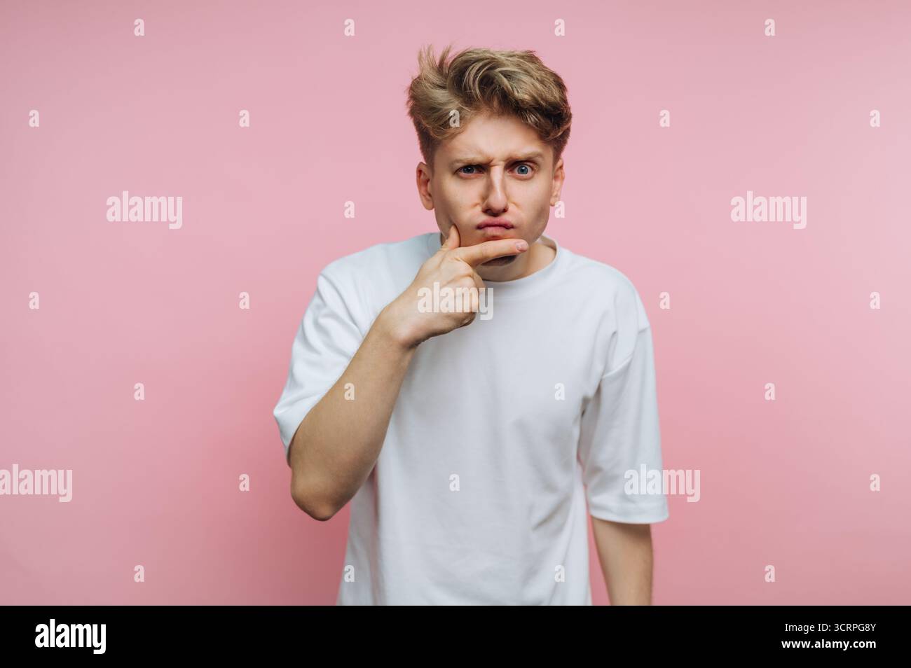 portrait du jeune homme fait une expression réfléchie tout en appuyant ses doigts sur son menton, symbolisant la confusion et la contemplation profonde sur le dos rose Banque D'Images