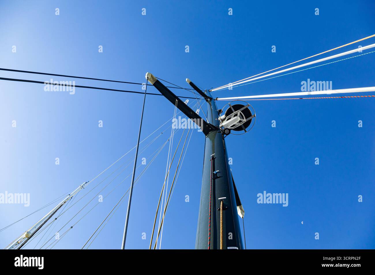 Le mât d'un yacht à voile avec un radar, des cordes à voile et une voile pliée, vu d'en bas contre le ciel. Banque D'Images