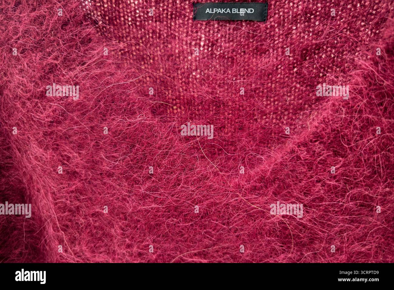 Pull à col en V Bordeaux brillant avec étiquette identifiant le texte anglais « Alpaca Blend ». La surface est moelleuse avec de longues fibres, caractéristique d'Alp Banque D'Images