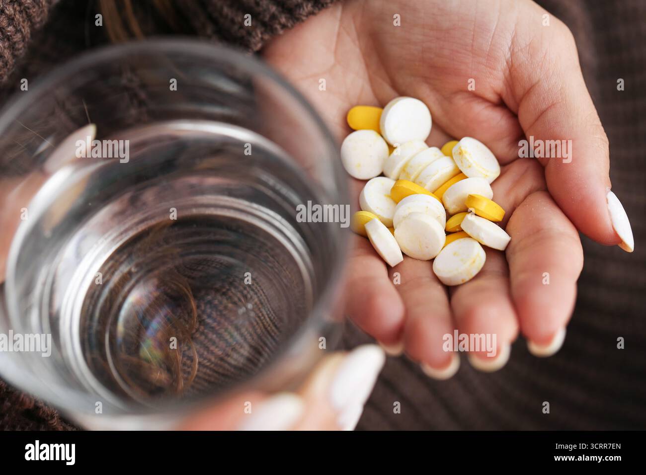 Femme tenant des pilules et un verre d'eau. Apport quotidien de suppléments à domicile. Mode de vie sain et routine de soins de santé. Médicaments et comprimés vitaminiques. Banque D'Images