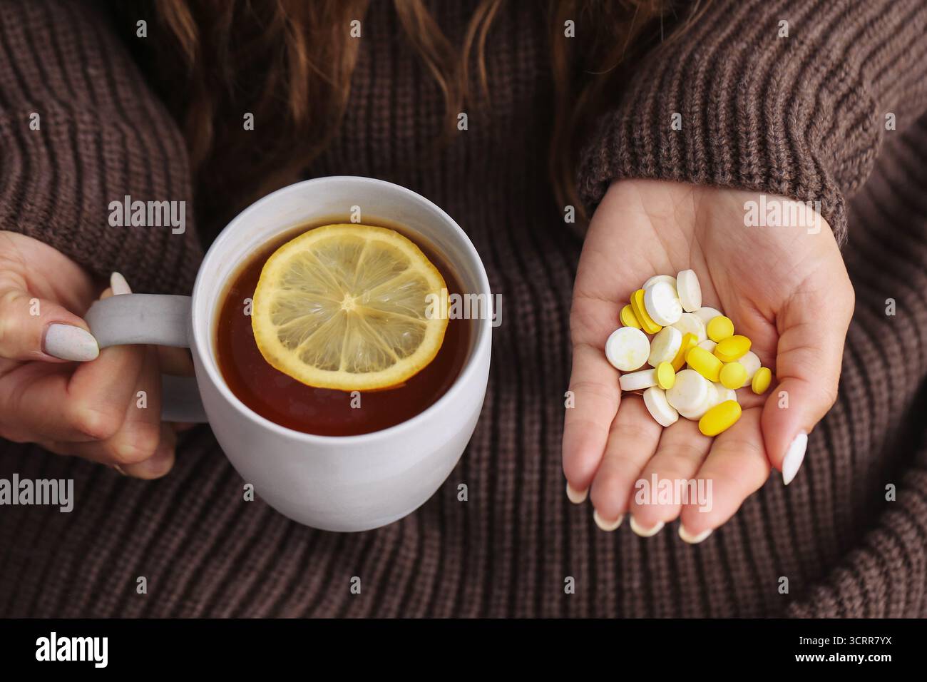 Femme tenant une tasse de thé chaud au citron et de vitamines à la main. Concept de médecine naturelle versus pilules pour le traitement de la grippe ou du rhume. Contexte de remède à domicile. Banque D'Images