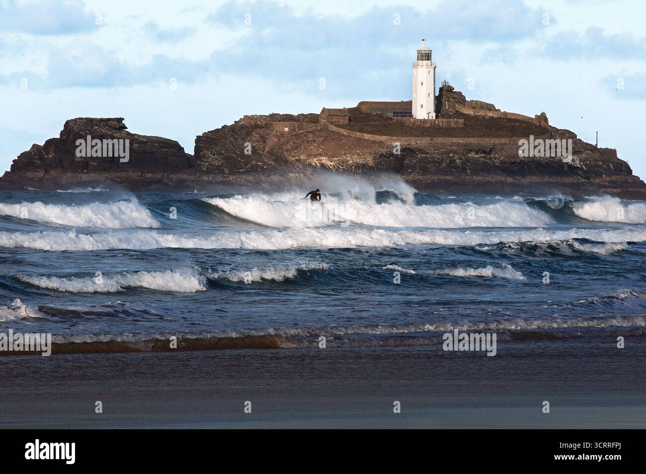 Un surfeur survole une vague près du phare de Godrevy à Cornwall, au Royaume-Uni. Ils apprécient les vagues et les beaux paysages. Banque D'Images