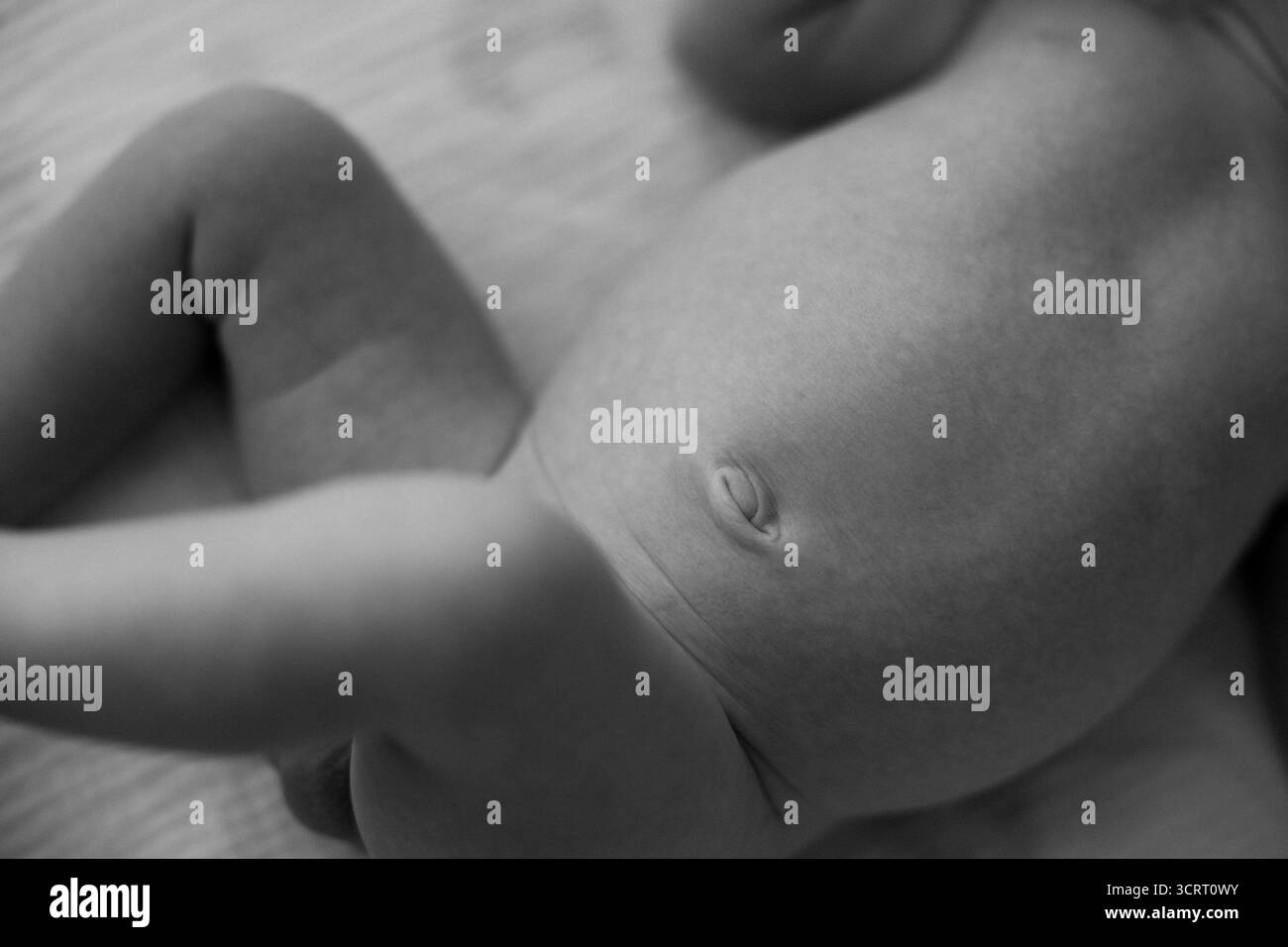 Un moment charmant révèle un bébé se relaxant, explorant curieusement une surface douce aux petits membres en mouvement doux, incarnant l’innocence et l’émerveillement. Banque D'Images