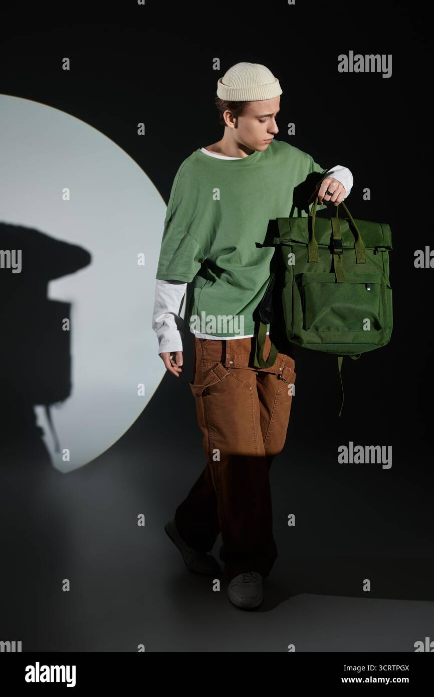 Un adolescent branché se promène en toute confiance avec un sac vert, mettant en valeur la culture urbaine de la jeunesse. Banque D'Images