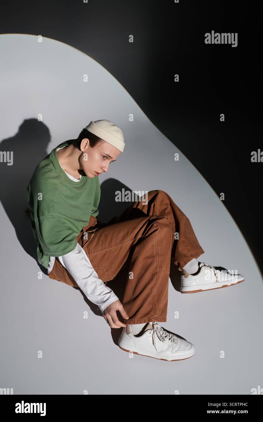 Un adolescent tendance ajuste ses baskets tout en étant assis sur une surface ondulée, incarnant la culture de la jeunesse. Banque D'Images