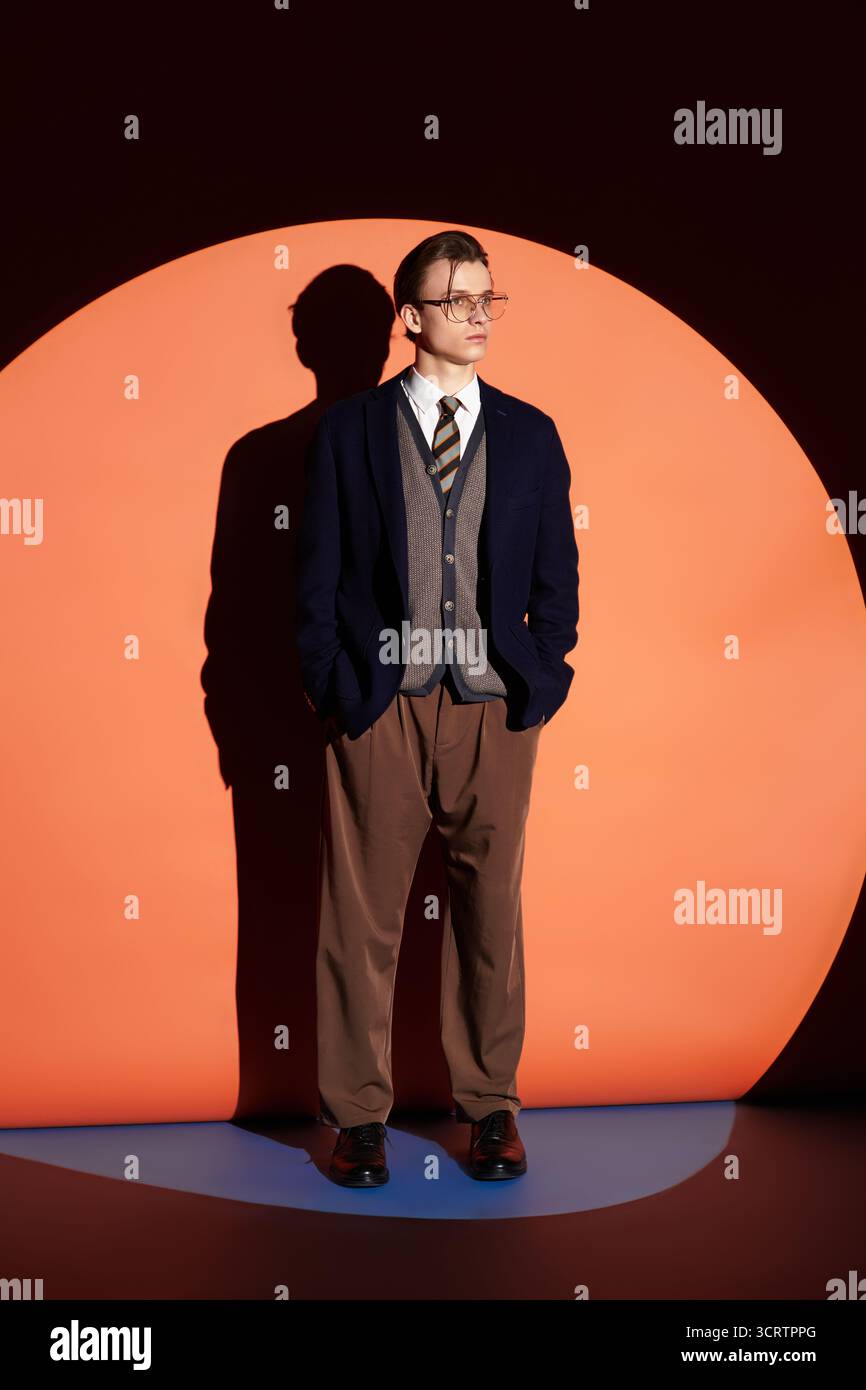 Un adolescent élégant pose contre un cercle orange vibrant, reflétant la culture moderne de la jeunesse. Banque D'Images