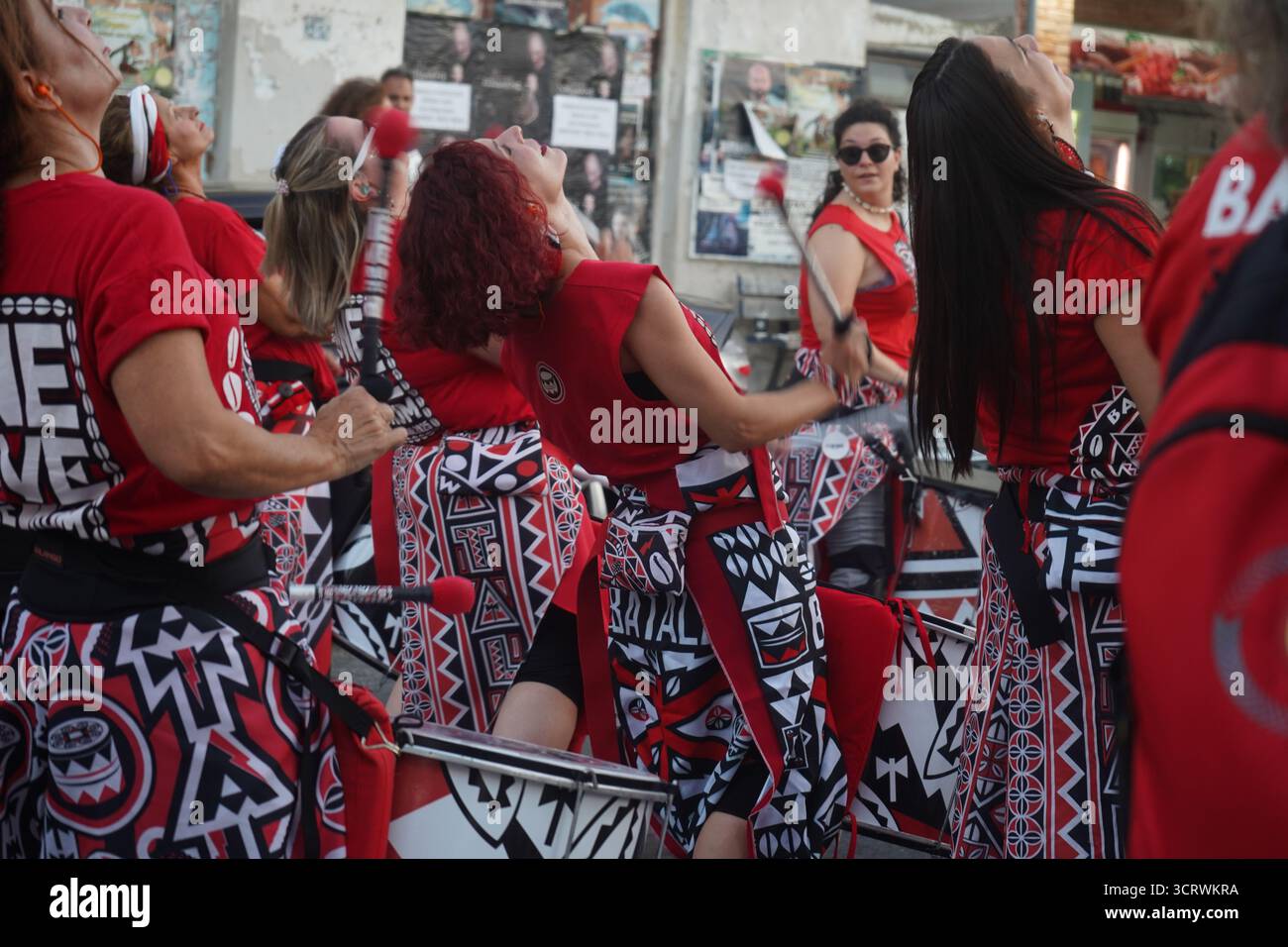 Le batteur passionné de Batala Creta en tenue rouge et noire joue avec une concentration intense, incarnant l'esprit du samba reggae au 3ème Festival Malevizi. Banque D'Images