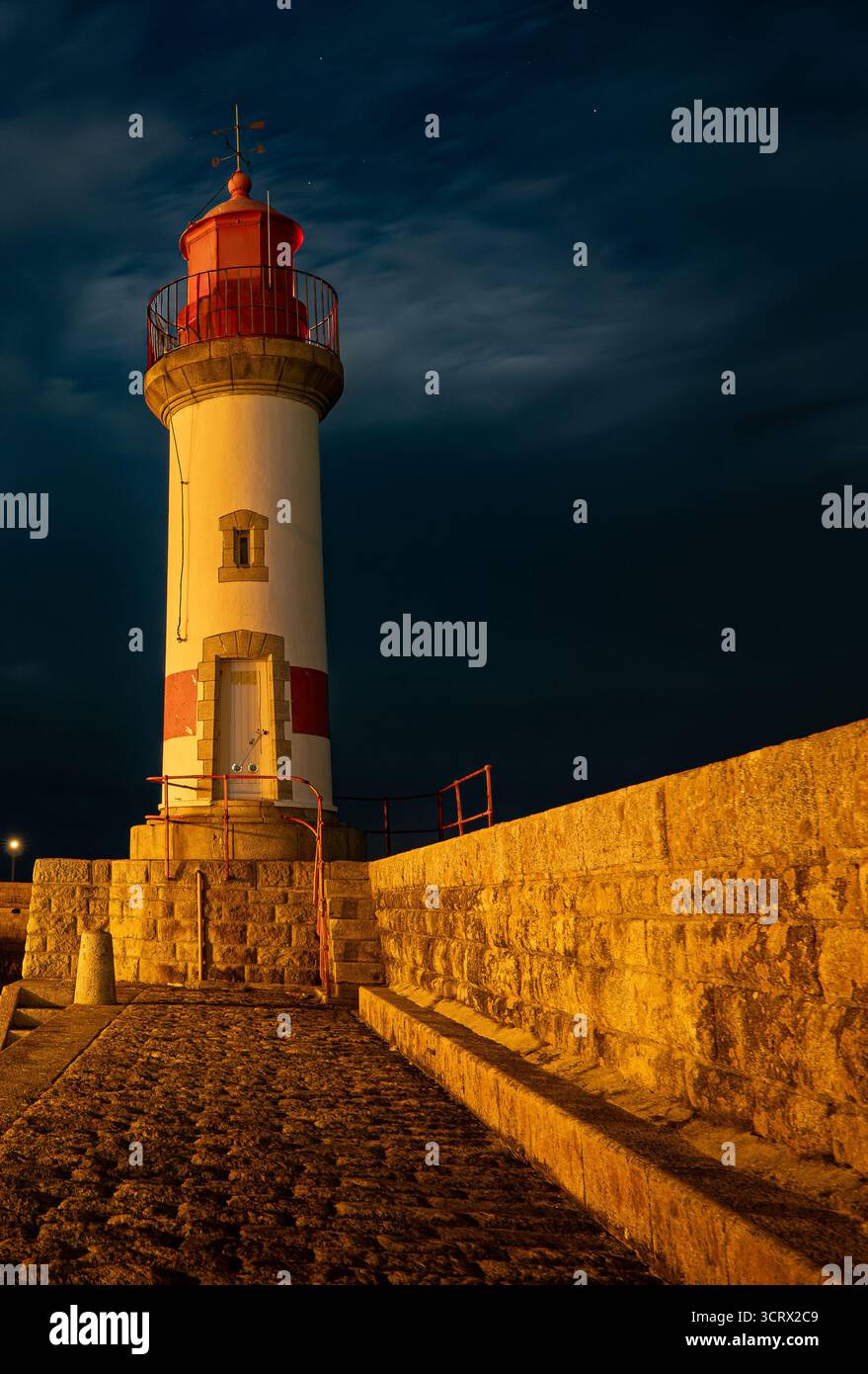 Un phare côtier frappant illuminé la nuit, baigné de lumière dorée contre un ciel bleu profond. Parfait pour les projets de voyage, éditoriaux ou beaux-arts Banque D'Images