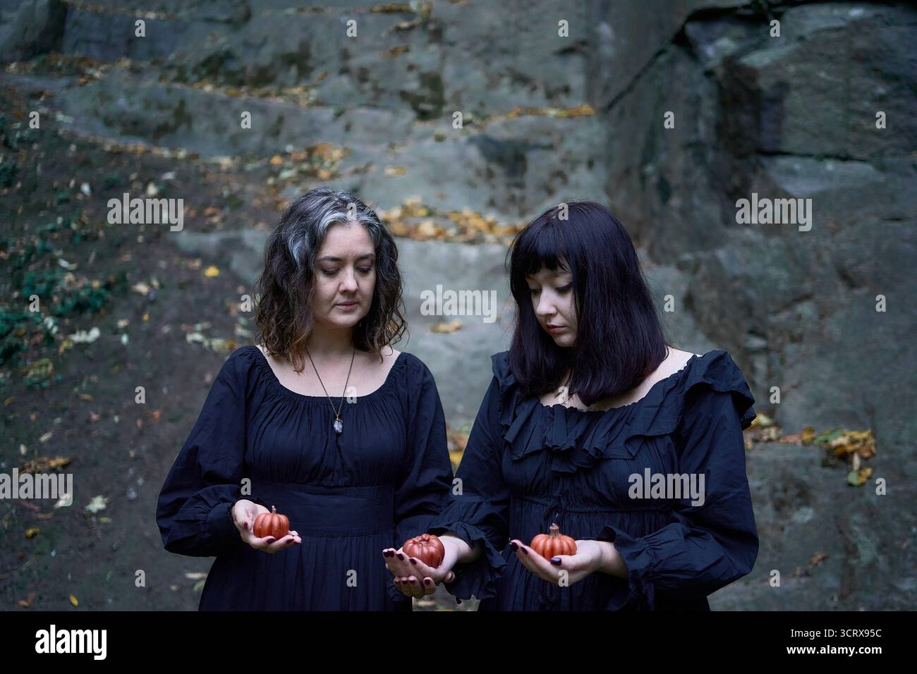 Deux femmes en robes longues noires près des rochers noirs sur Halloween avec des bougies en forme de citrouilles, effectuant un rituel de sorcière, sorcière moderne Banque D'Images