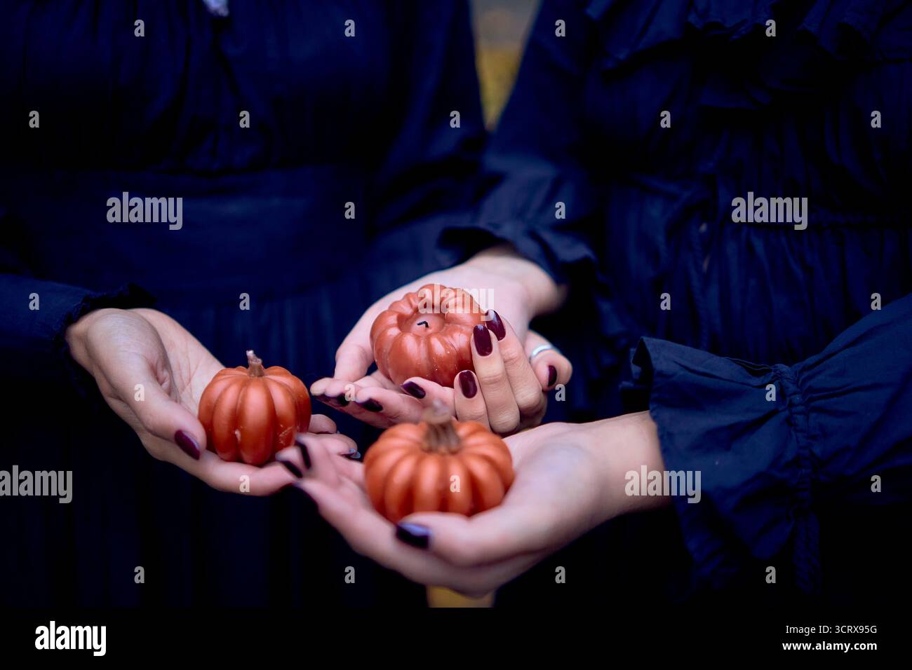 Deux femmes en robes longues noires près des rochers noirs sur Halloween avec des bougies en forme de citrouilles, effectuant un rituel de sorcière, sorcière moderne Banque D'Images