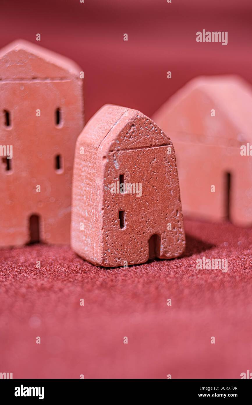 Une image en gros plan de trois petits modèles de maison en argile placés sur une surface rouge texturée. La faible profondeur de champ souligne la maison miniature centrale Banque D'Images