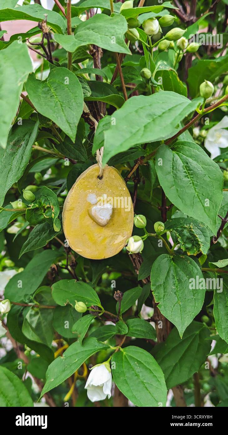 Artisanat d'oeufs de Pâques en céramique suspendu parmi les fleurs blanches dans la lumière du printemps Banque D'Images