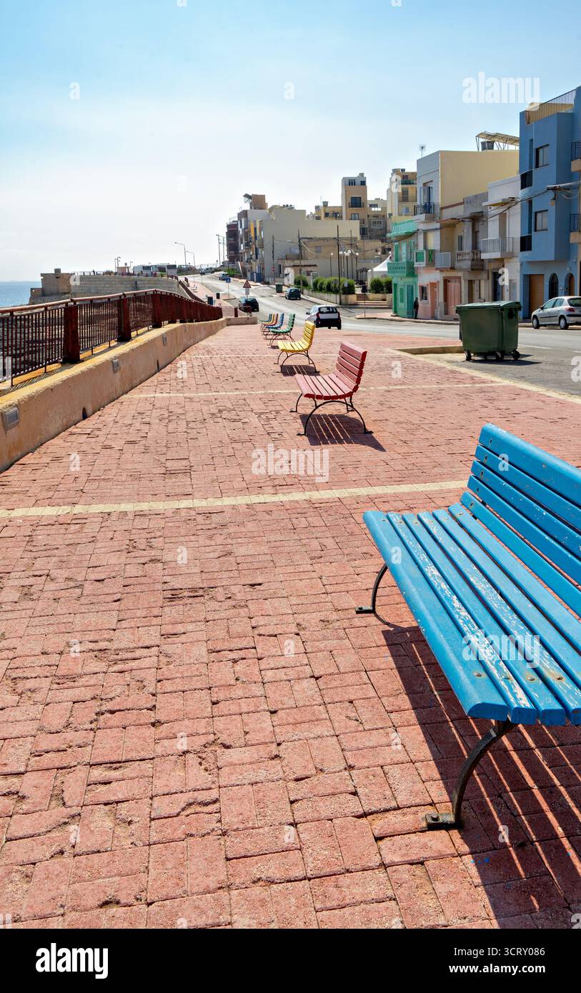 Promenade de bord de mer de Xghajra Malte avec banc bleu et vue sur la ville côtière Banque D'Images