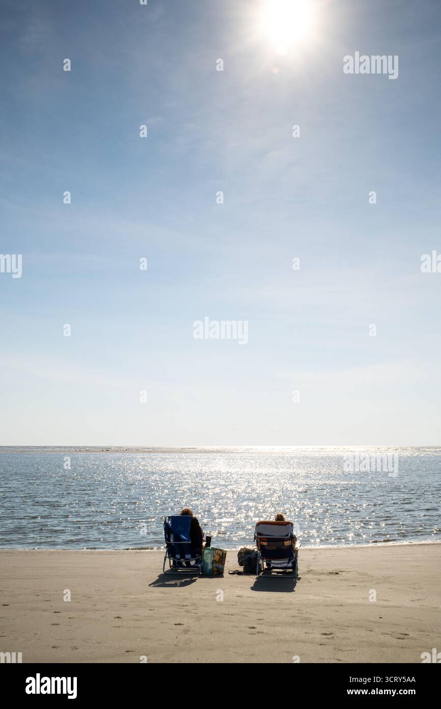 Deux personnes dans des chaises de plage sur l'île de Palms Caroline du Sud // SULLIVANS ISLAND, Caroline du Sud — deux personnes se détendent dans des chaises de plage sur la rive sablonneuse de l'île de Sullivans, face à l'océan Atlantique. Cette île barrière est une destination populaire située à l'entrée du port de Charleston dans le comté de Charleston. Sullivans Island est connue pour ses larges plages et son importance historique. Il offre des vues panoramiques le long de la côte de Caroline du Sud, attirant les visiteurs pour les loisirs et la détente. L'île fait partie de la région métropolitaine de Charleston. Banque D'Images