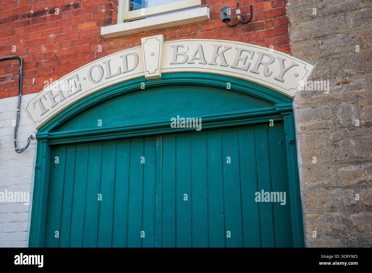 Historique 'The Old Bakery' signe au-dessus des portes en bois sarcelle dans le bâtiment de brique vintage à Allngton, Bridport, Dorset, Banque D'Images