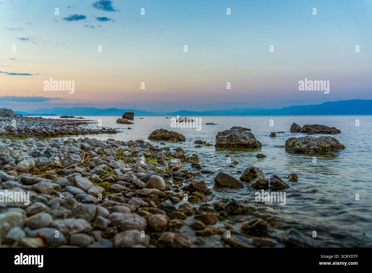 Rivage rocheux du lac Ohrid près de Pogradec Albanie au coucher du soleil coloré avec de l'eau calme, des pierres et des montagnes au loin Banque D'Images