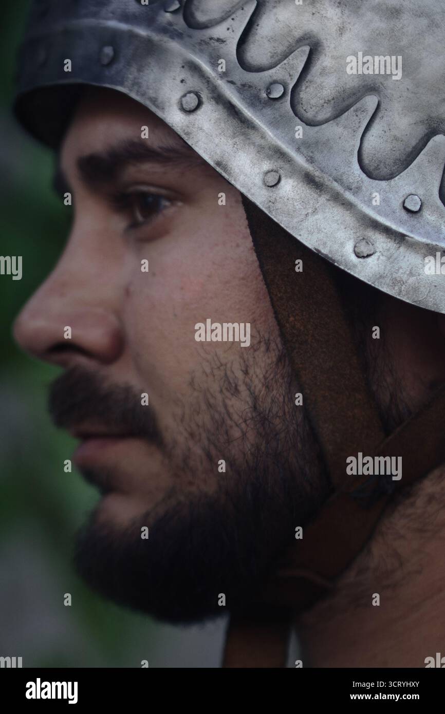 Gros plan d'un homme en armure médiévale criant avec intensité lors d'une reconstitution ou d'une scène de bataille. L'expression dramatique et le casque. Banque D'Images