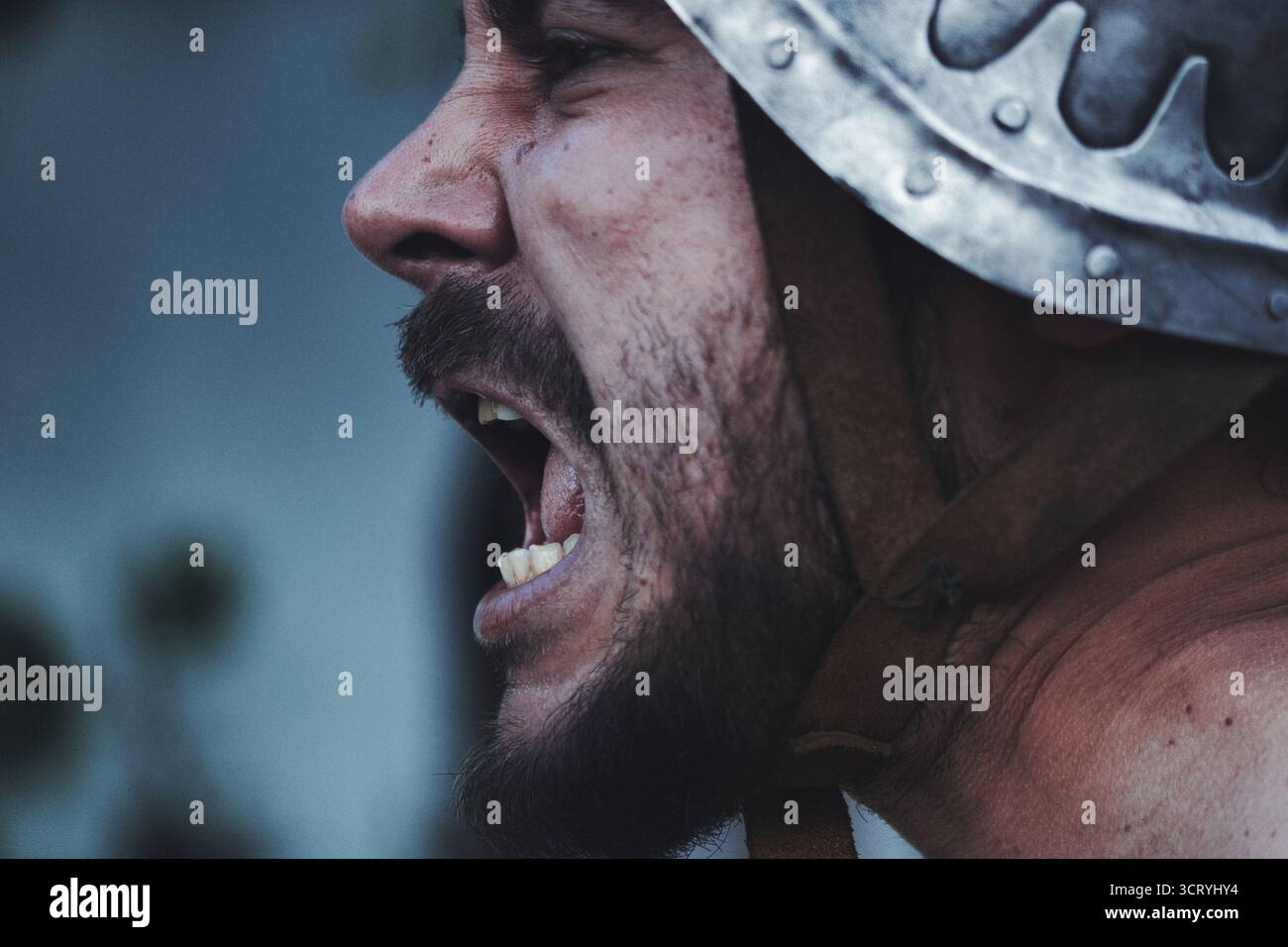Gros plan d'un homme en armure médiévale criant avec intensité lors d'une reconstitution ou d'une scène de bataille. L'expression dramatique et le casque. Banque D'Images
