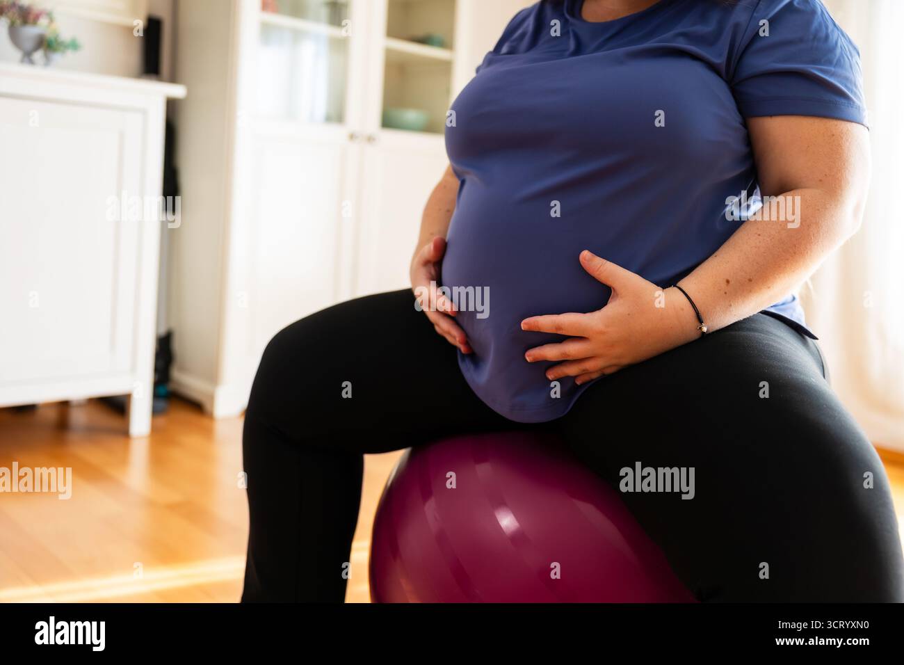Gros plan d'une femme enceinte assise sur le ballon d'exercice avec les mains sur le ventre. Style de vie. Grossesse. Banque D'Images