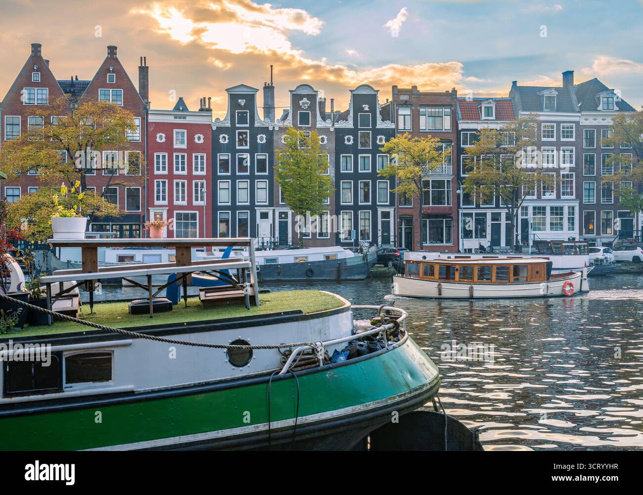 Coucher de soleil d'automne à Amsterdam, le front de mer de la rivière Amstel avec maisons de canal traditionnelles et péniches Banque D'Images