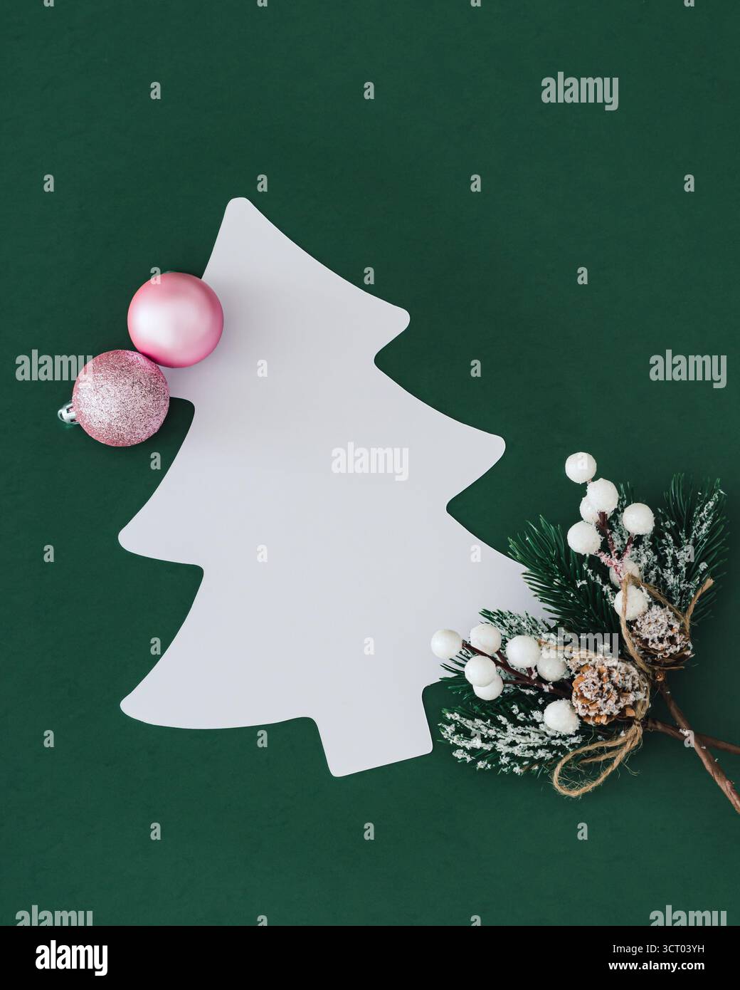 Composition festive minimaliste avec des boules de Noël roses, des branches décoratives et un espace de copie en forme d'arbre sur fond vert. Concept créatif de Noël. Banque D'Images