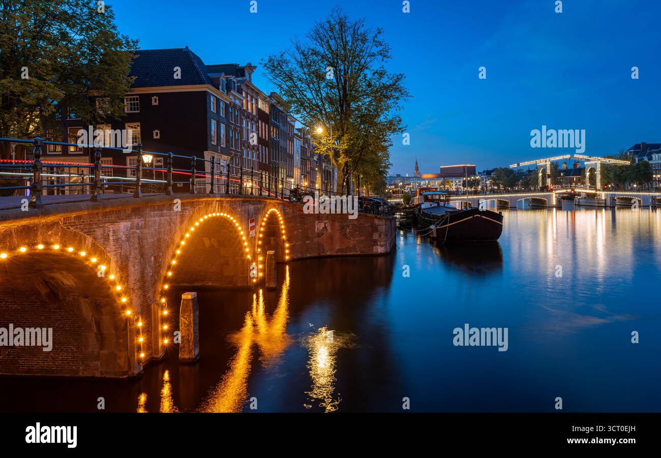 Heure bleue à Amsterdam avec Magere Brug illuminé (Pont maigre) sur la rivière Amstel, canal et maisons traditionnelles Banque D'Images