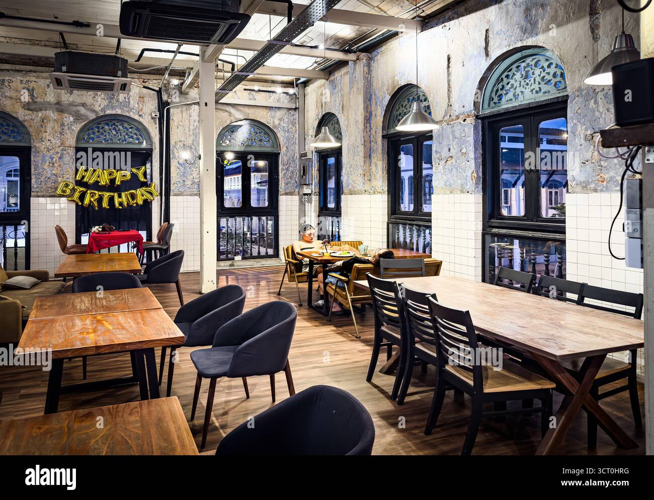 Intérieur rustique de restaurant avec décorations d'anniversaire, avec tables et chaises en bois, tuyaux apparents et fenêtres cintrées restaurant à Ipoh Malaisie - Image de stock capturée avec un smartphone