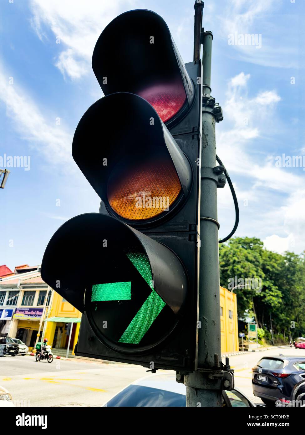 Une vue rapprochée d'un feu de circulation montrant une flèche de filtre verte sur une toile de fond de bâtiments urbains et un ciel bleu clair ipoh malaysia - Image de stock capturée avec un smartphone