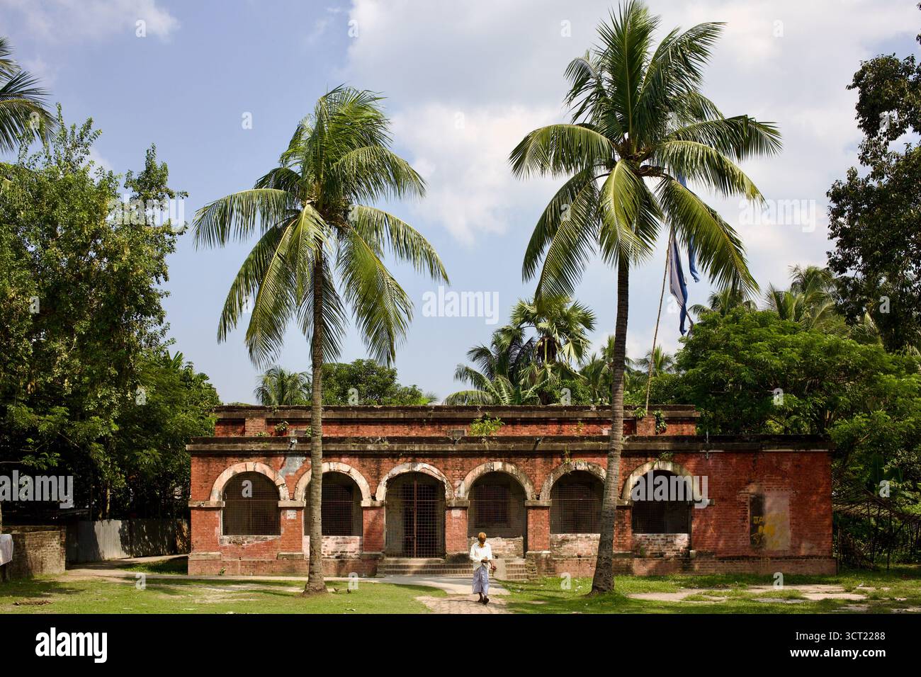 Ancien bâtiment en briques rouges avec fenêtres cintrées et palmiers à Kushtia, au Bangladesh, typique de l'architecture coloniale tardive dans le Bengale rural. Banque D'Images