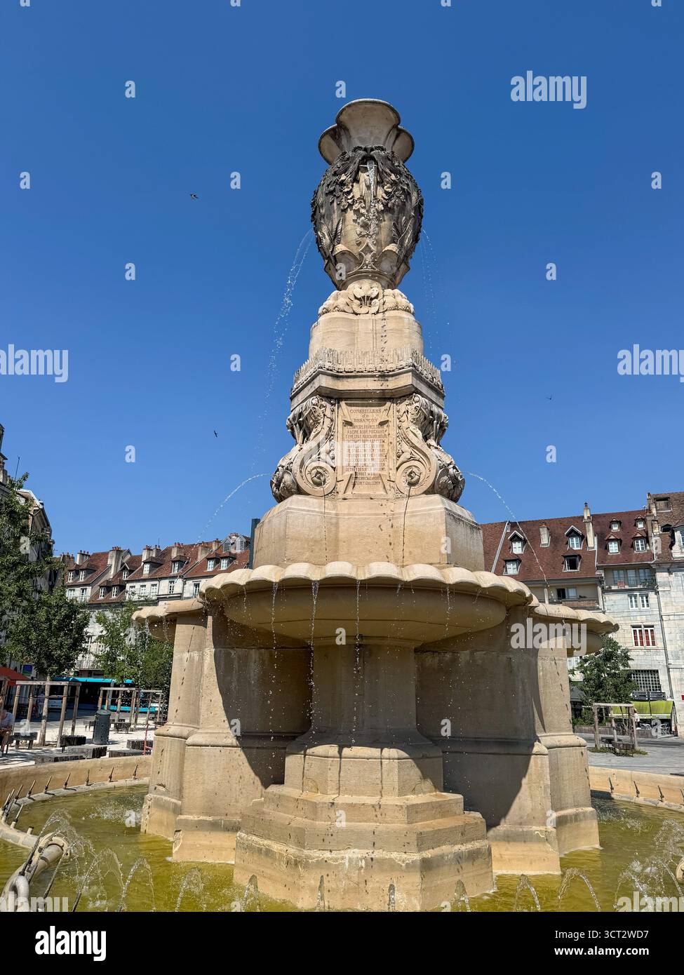 Vue frontale basse de Fontaine des Dames sur la place de la Révolution, Besançon, avec bâtiments historiques et ciel bleu d'été en arrière-plan. - Image de stock capturée avec un smartphone
