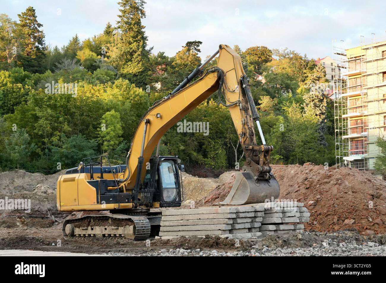excavatrice sur un chantier de construction sur un fond d'arbres verts Banque D'Images