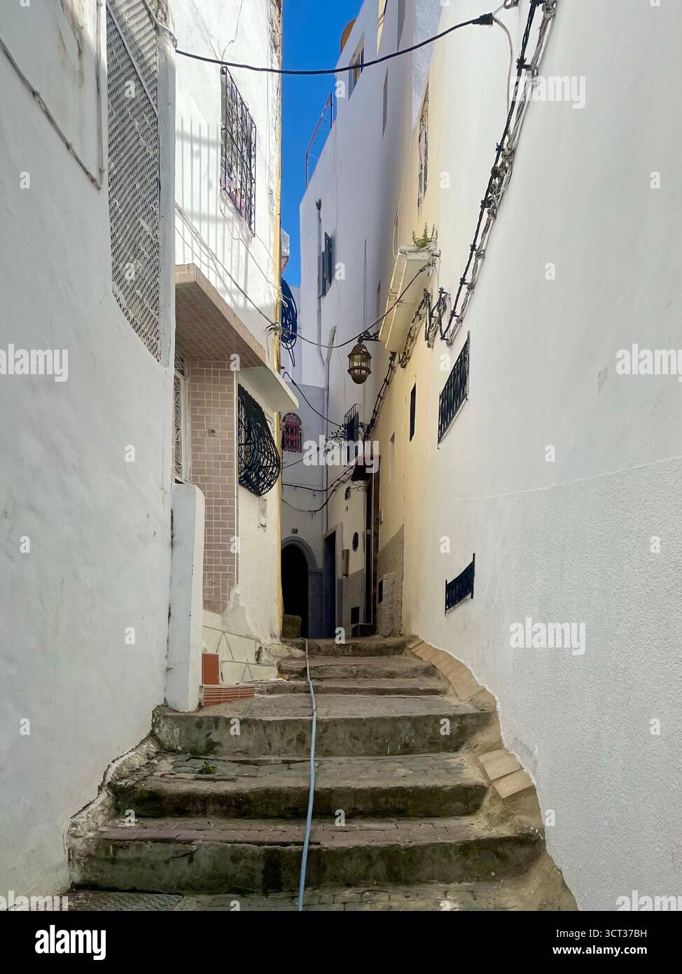 Ruelle en pente dans la vieille médina avec des façades en couches, des marches carrelées et un mélange de textures vieillies sous un ciel partiellement nuageux. Tanger, le 7 juin 2024 Banque D'Images