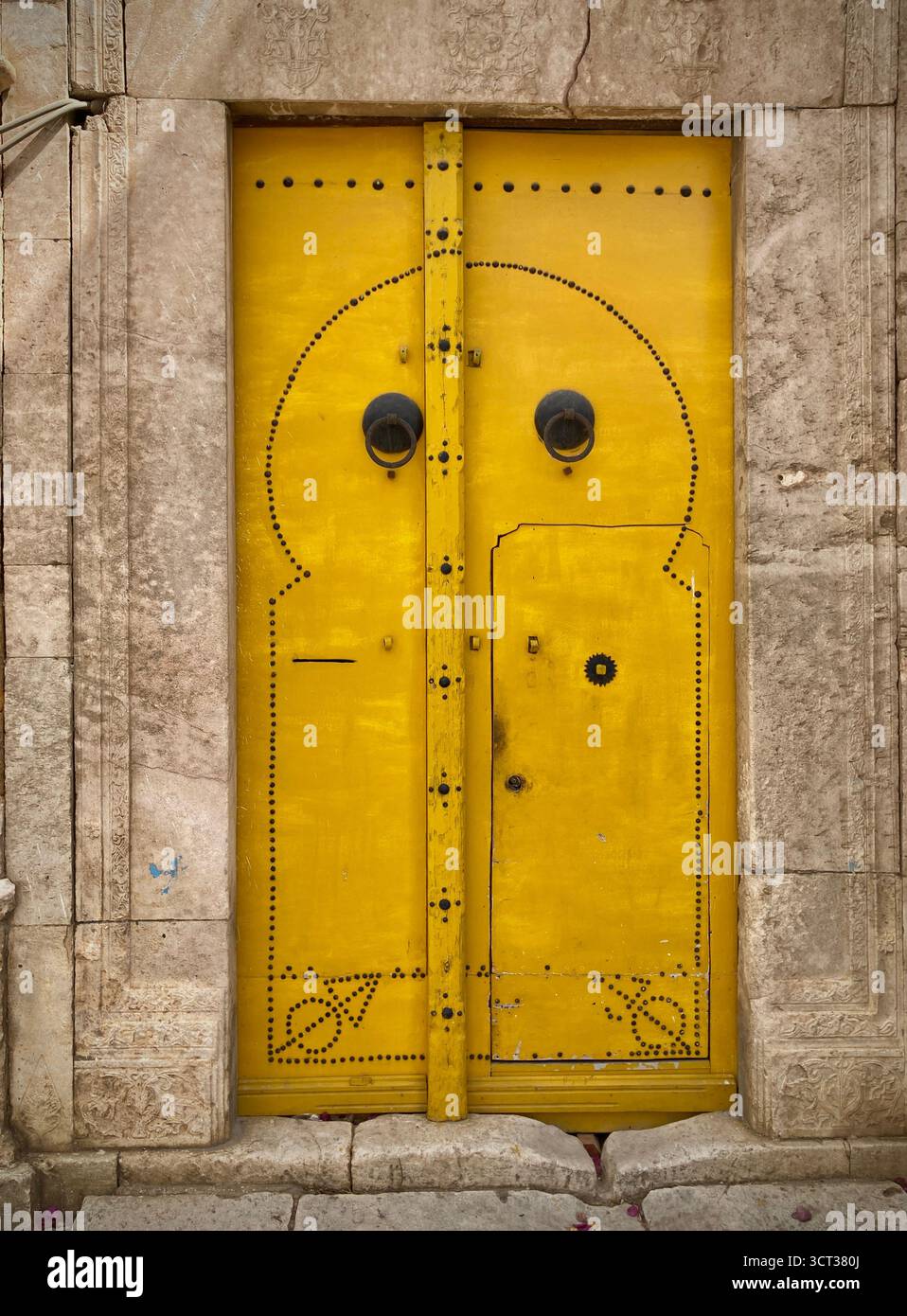 Porte jaune traditionnelle dans l'ancienne médina de Tunis, Tunisie. Design arqué, motifs d'ongles noirs et frappeurs en métal. Capturé le 22 septembre 2025. Banque D'Images