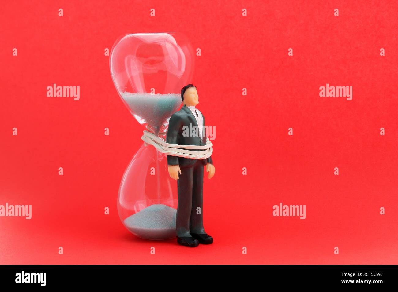 Exécutif attaché avec un élastique à un sablier, un temps limité comme un obstacle à l'accomplissement d'une tâche Banque D'Images