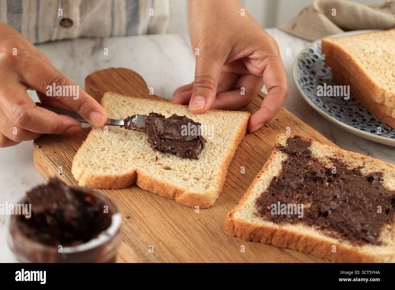 Étaler le beurre de noix au chocolat sur du pain blanc tranché ou du Roti Tawar. Les mains féminines enduisent le chocolat tartiné sur le pain sandwich. Préparer le déjeuner ou les Breakfas Banque D'Images