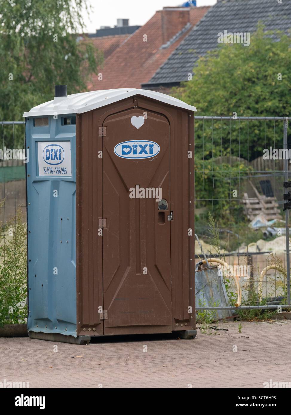 Cabine de toilette portable Dixi placée sur un chantier de construction dans un quartier résidentiel avec des maisons et des matériaux de jardin en arrière-plan Banque D'Images